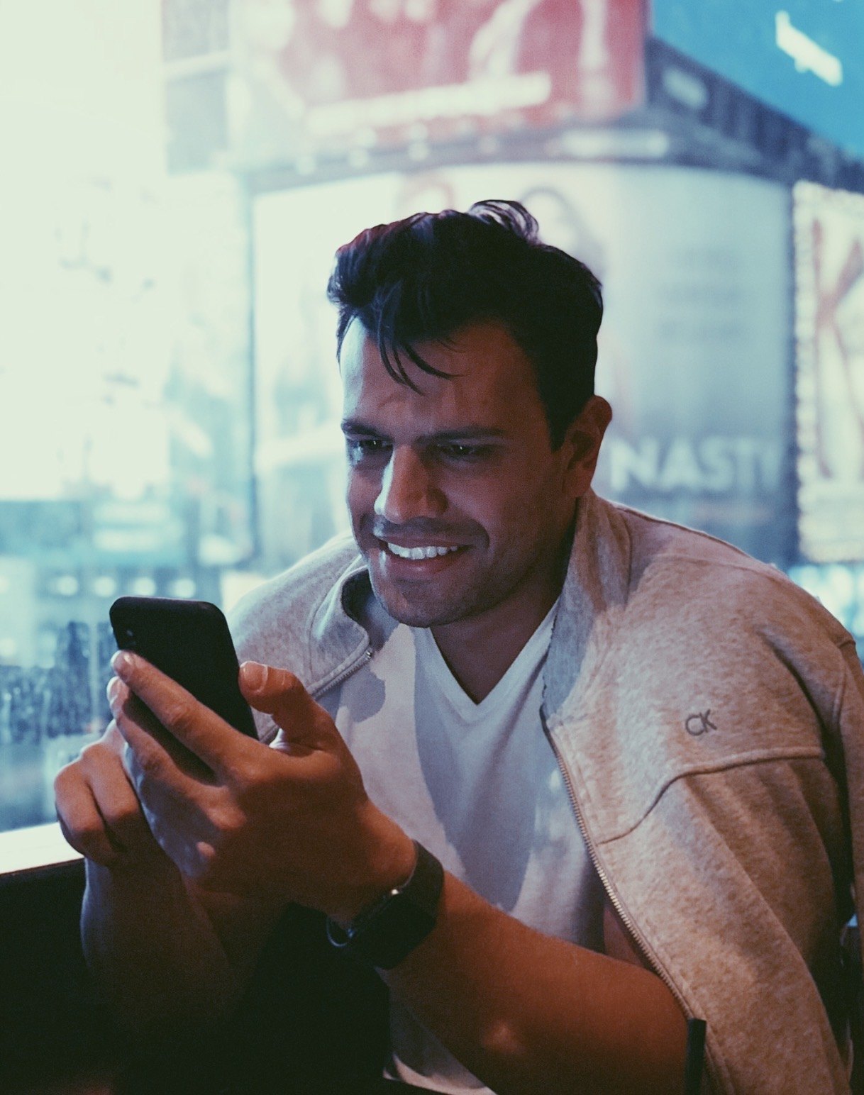 Daniel Malinoski sorrindo enquanto olha o celular, com luzes da cidade ao fundo